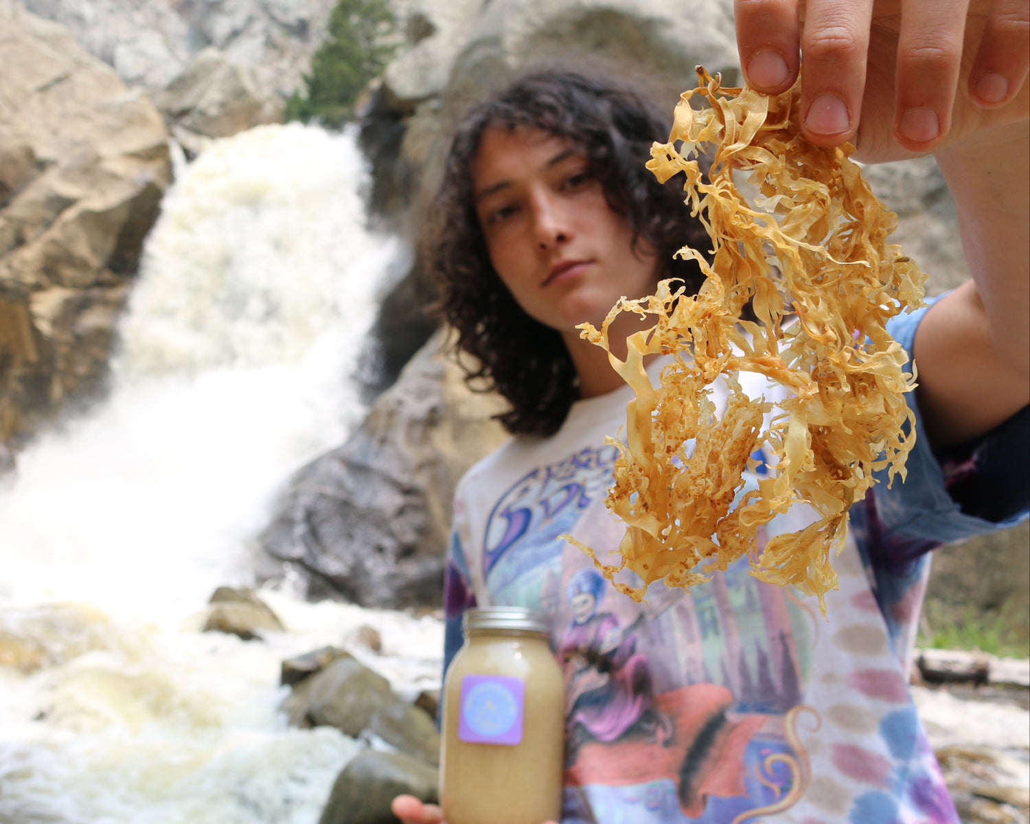 Person holding a jar of water and gold leaf with a waterfall in the background